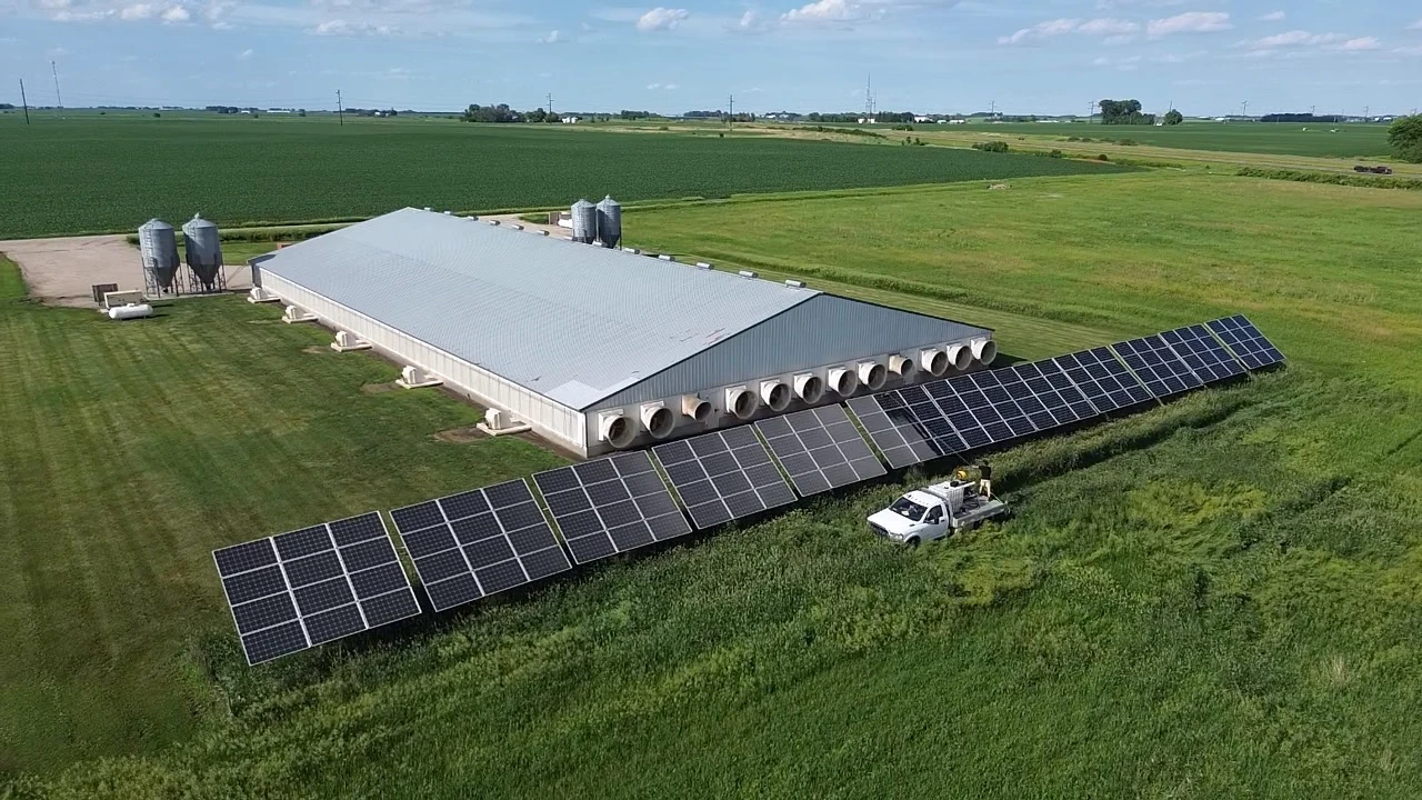 Aerial view of a farm building with ground-mounted solar panels and surrounding fields
